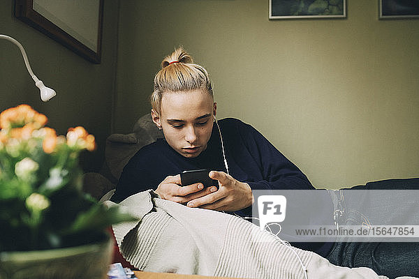 Männlicher Teenager benutzt Smartphone  während er zu Hause im Bett liegt