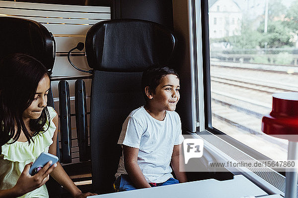 Boy looking through window while sitting with sister in train