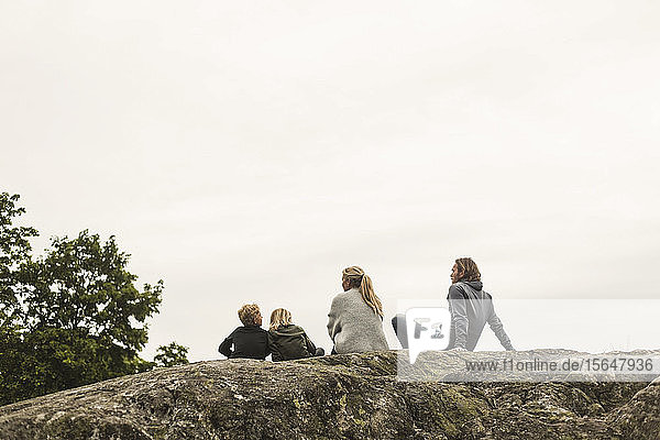 Familie ruht gemeinsam auf einer Felsformation vor klarem Himmel