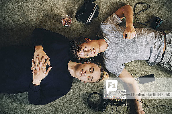 Directly above shot of male teenagers with closed eyes listening music while lying on carpet at home