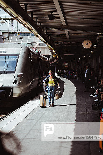 Glückliche Frau in voller Länge mit Gepäck läuft auf dem Bahnsteig