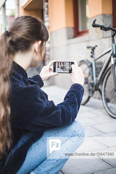 Young woman photographing bicycle on footpath