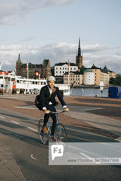 Fahrrad fahrender Geschäftsmann in voller Länge auf der Straße in der Stadt gegen den Himmel