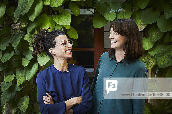 Lächelnde Architektinnen gegen Kletterpflanzen im Hinterhof
