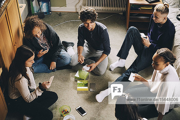 High angle view of male and female friends playing board game while sitting in bedroom at home