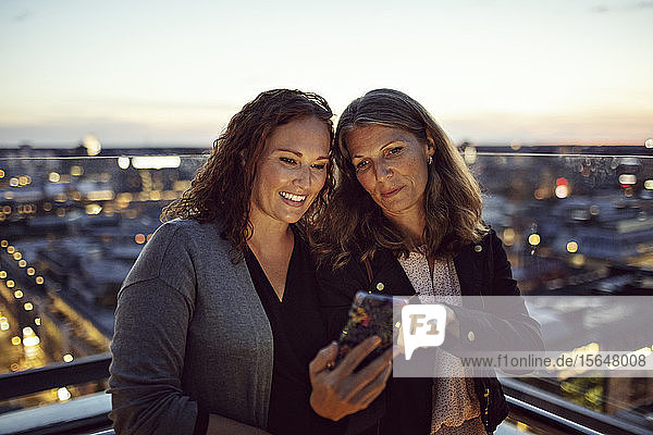 Geschäftsfrauen  die nach der Arbeit auf der Terrasse stehen und sich am Smartphone selbstständig machen