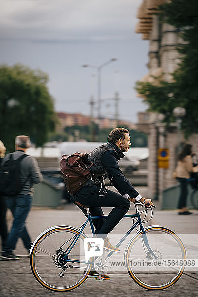 Seitenansicht eines selbstbewussten Geschäftsmannes  der auf der Straße in der Stadt Fahrrad fährt