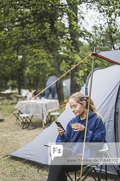 Teenage girl using mobile phone while having coffee against tent