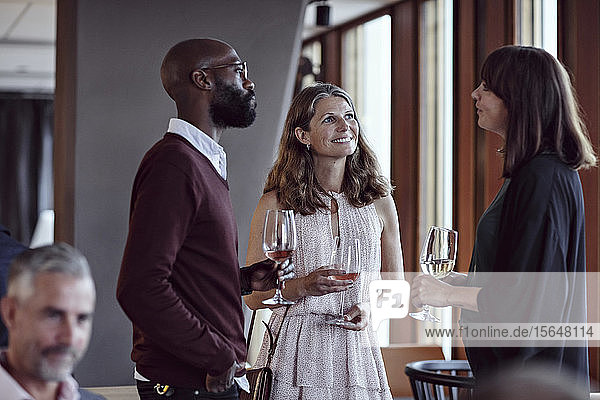 Male and female colleagues talking while enjoying drinks in party after work