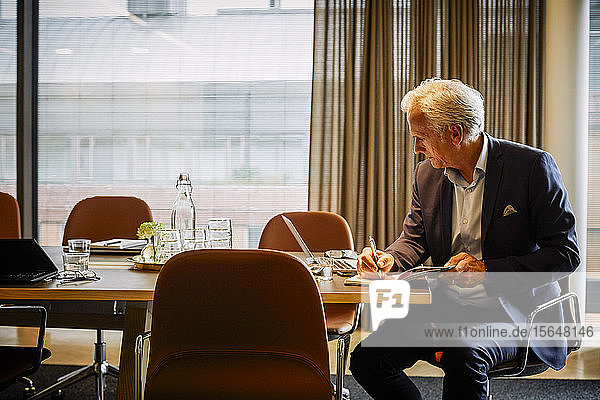 Reife Juristen schreiben im Tagebuch  während sie ihren Laptop am Konferenztisch im Sitzungssaal benutzen