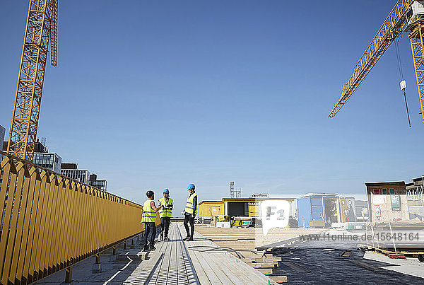 Male and female engineers discussing at construction site against blue sky