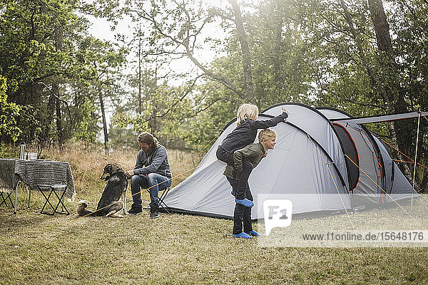 Geschwister spielen  während der Mann mit dem Hund im Zelt am Campingplatz sitzt