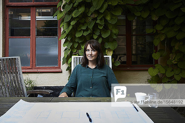 Porträt einer selbstbewussten Architektin mit Blaupause am Tisch im Hinterhof