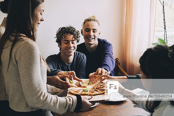Teenage girl serving pizza to happy friends at dining table