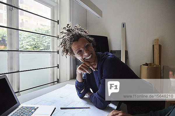 Lächelnde junge Architektin lehnt sich im Büro auf den Tisch