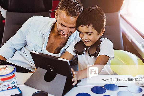 Lächelnder Vater und Sohn benutzen digitales Tablet  während sie im Zug sitzen