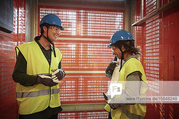 Lächelnde Ingenieurinnen diskutieren  während sie auf der Baustelle im Lastenaufzug stehen