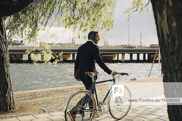 Geschäftsmann zu Fuß mit dem Fahrrad auf dem Fußweg am Kanal in der Stadt