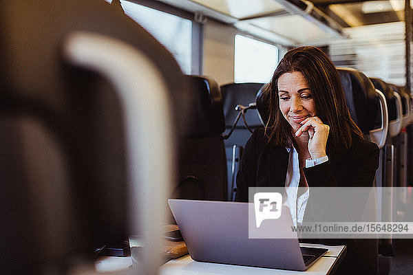 Lächelnde Geschäftsfrau benutzt Laptop  während sie im Zug sitzt