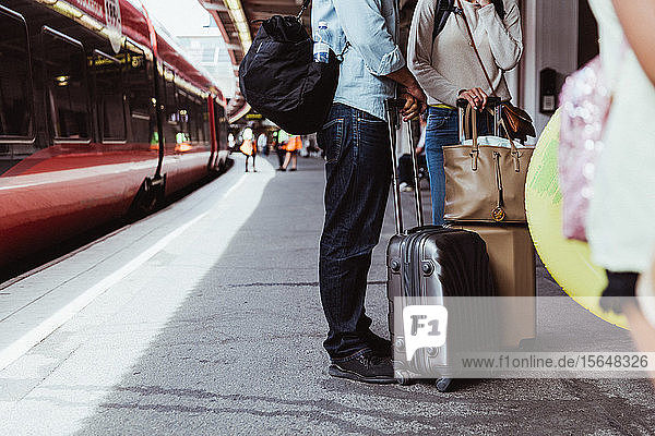 Niedriger Abschnitt eines Paares mit Gepäck  das auf dem Bahnsteig des Bahnhofs steht