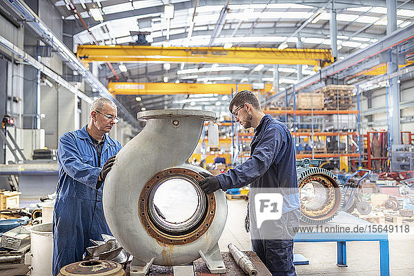 Engineer and apprentice inspecting snail shaded pump housing in electrical engineering factory