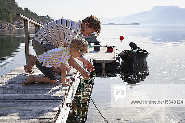 Father teaching son to tie boat to pier  Norway