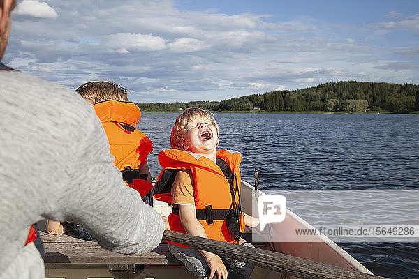 Erwachsener segelt mit aufgeregten Jungen auf einem Boot auf dem See  Finnland