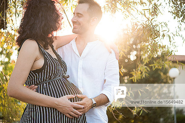 Man smiling and touching belly of pregnant wife in park