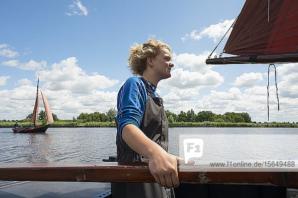 Girl stands at helm of large flat-bottom traditional sailing ship