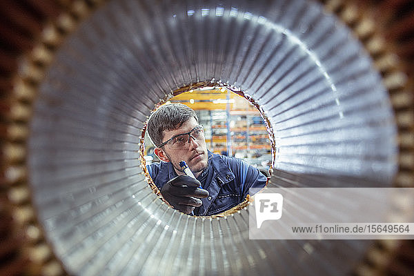 Apprentice electrical engineer inspecting winding on generator stator in electrical engineering factory
