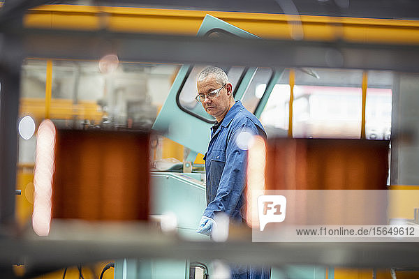 Electrical engineer operating copper wire winding machine in electrical engineering factory