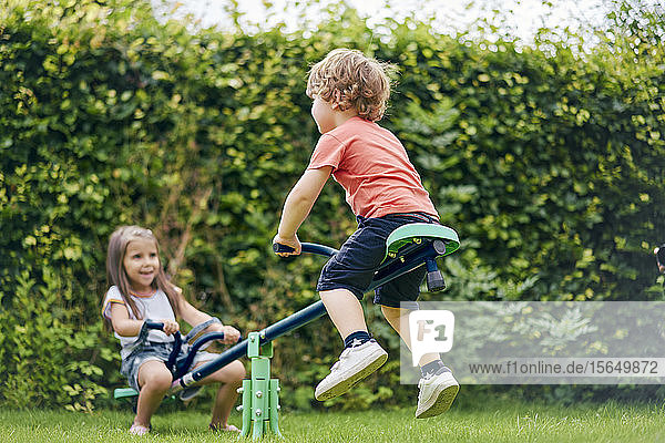 Mädchen und Junge auf Spielzeugwippe im Garten