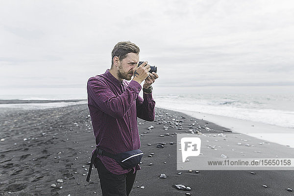 Mann beim Fotografieren am Strand in Island