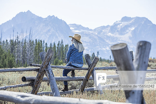 Frau sitzt auf einem Holzzaun vor den Bergen in Stanley  Idaho  USA