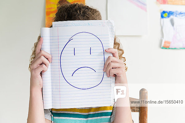 Mädchen hält Notizblock mit Zeichnung eines traurigen Gesichts