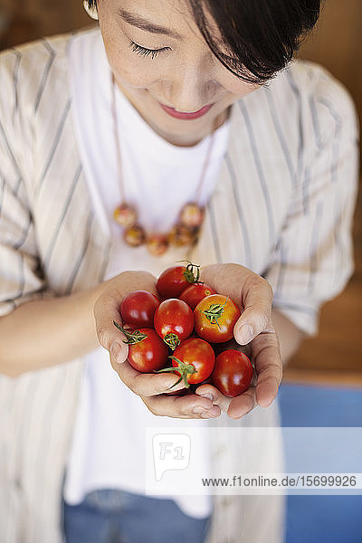 Nahaufnahme einer Japanerin  die frisch gepflückte Tomaten hält.