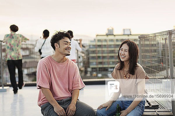 Lächelnde junge Japaner und Japanerinnen sitzen auf einem Dach in einer städtischen Umgebung.