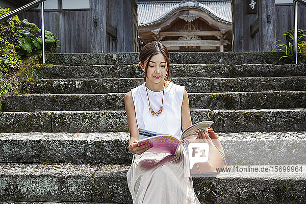 Japanerin  die auf Stufen vor einem buddhistischen Tempel sitzt.