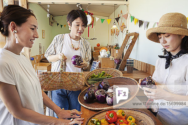 Japanische Frau mit Hut  die in einem Hofladen arbeitet und zwei weibliche Kunden bedient.