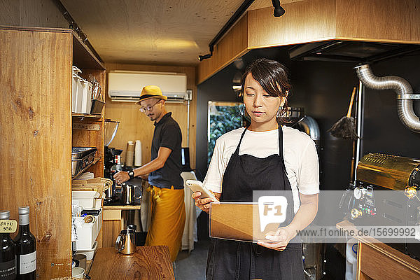 Japanerin und Japaner arbeiten in einem Öko-Café  bereiten Kaffee zu und benutzen ein Mobiltelefon.