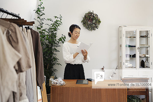Japanerin  die in einer kleinen Modeboutique steht und eine Broschüre liest.