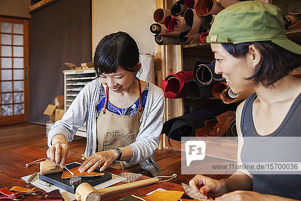 Zwei Japanerinnen  die an einem Tisch sitzen und in einem Ledergeschäft arbeiten.