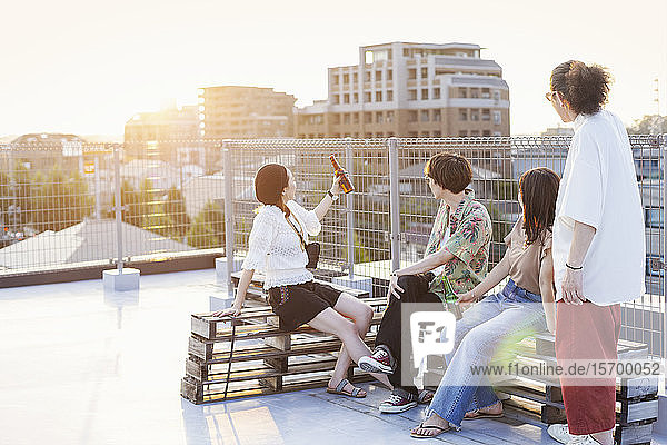 Gruppe junger japanischer Männer und Frauen  die auf einem Dach in einer städtischen Umgebung sitzen.