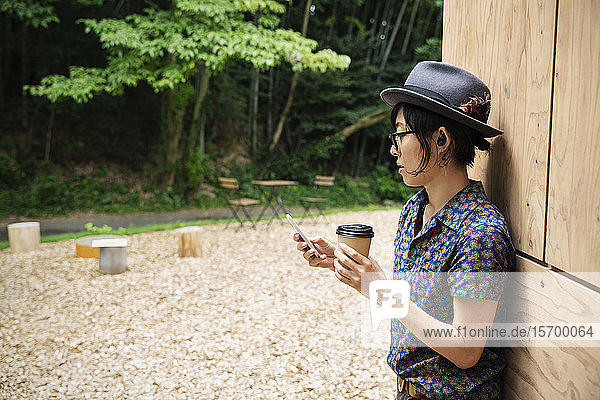 Japanerin mit Brille und Hut steht vor dem Eco Cafe und hält einen Pappbecher.
