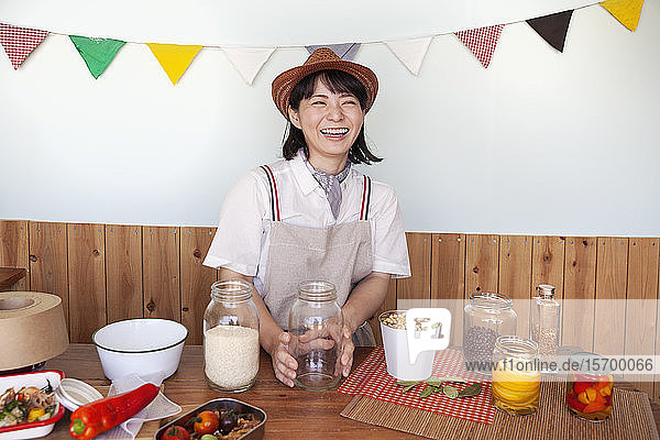 Japanerin mit Hut  die in einem Hofladen mit einer Auswahl an Lebensmitteln und Gewürzen in Gläsern steht.