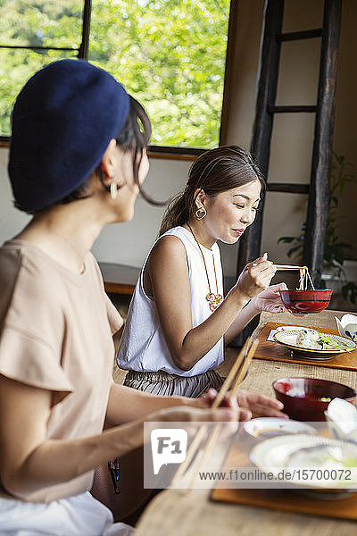 Zwei Japanerinnen sitzen an einem Tisch in einem japanischen Restaurant und essen.