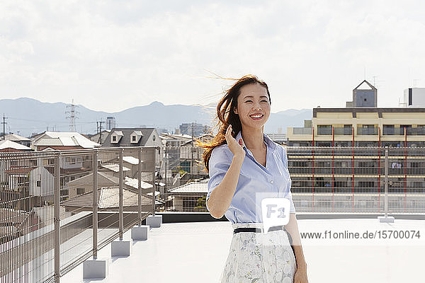Young Japanese woman standing on a rooftop in an urban setting  looking at camera.