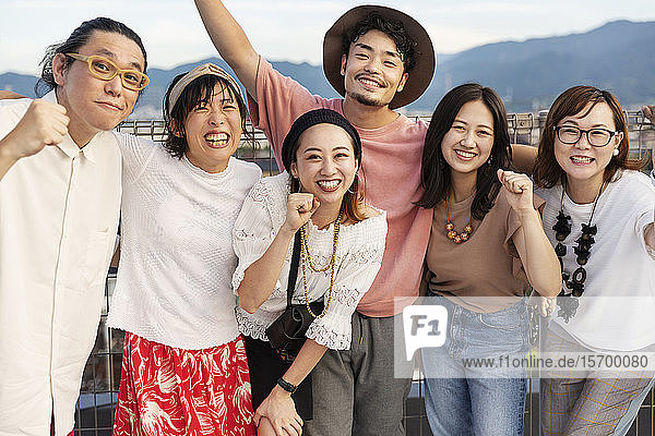 Lächelnde Gruppe junger japanischer Männer und Frauen  die auf einem Dach in einer städtischen Umgebung stehen.