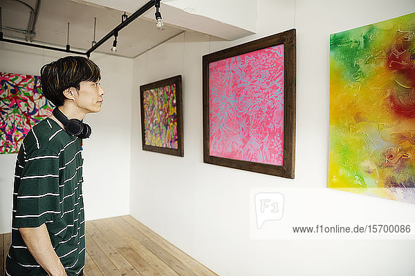 Japanischer Mann mit Kopfhörer betrachtet abstrakte Malerei in einer Kunstgalerie.