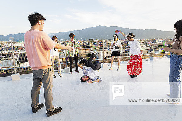 Gruppe junger japanischer Männer und Frauen  die auf einem Dach in einer städtischen Umgebung tanzen.